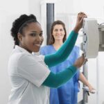 Radiologic technologist adjusting X-ray machine with patient standing behind