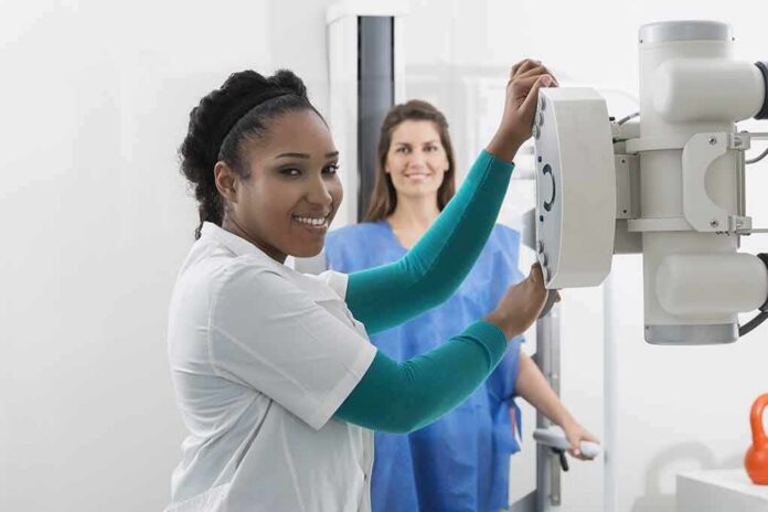 shutterstock_590176667 Radiologic technologist adjusting X-ray machine with patient standing behind