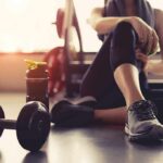 person resting on gym floor with dumbbell and water bottle
