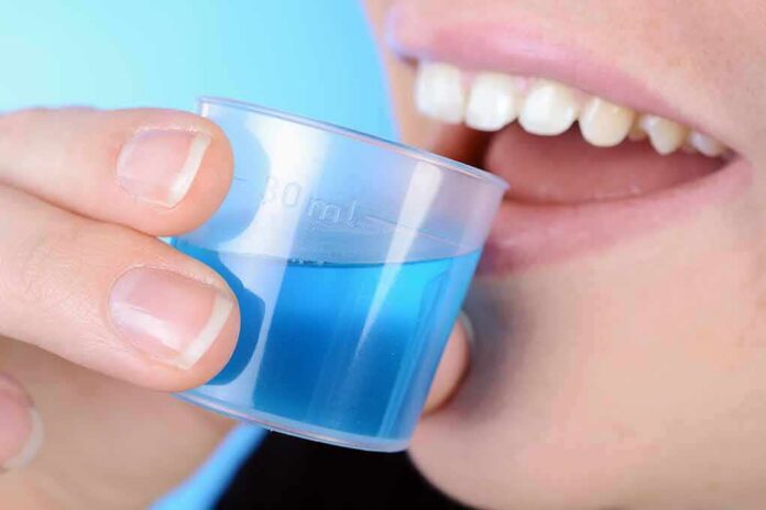 person holding a small cup of blue mouthwash near their teeth
