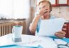 Older woman covering her face while reading a document at a kitchen table