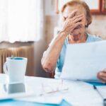 Older woman covering her face while reading a document at a kitchen table