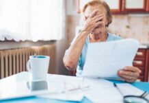 Older woman covering her face while reading a document at a kitchen table