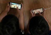 Two children playing mobile games side by side on the floor