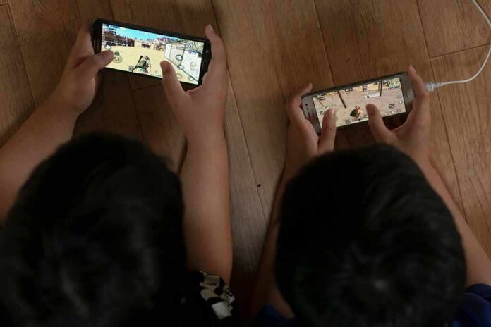 Two children playing mobile games side by side on the floor