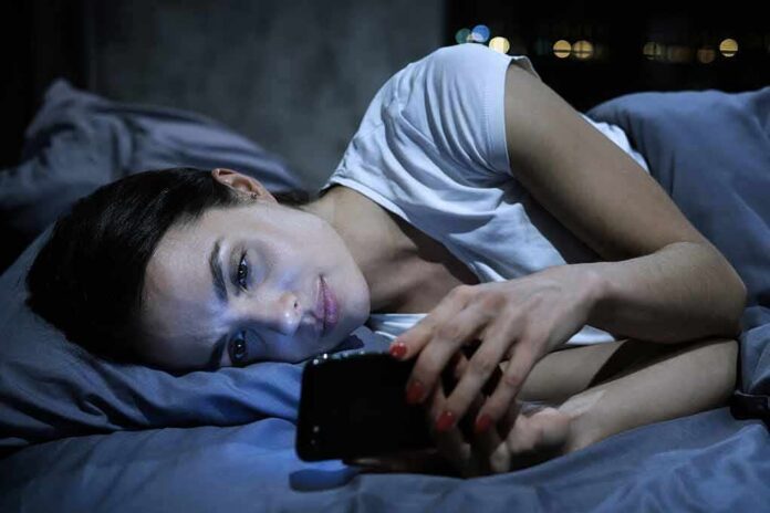 shutterstock_1208195308-2 Woman lying in bed looking at a smartphone