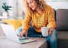Woman on a couch using a laptop and holding a mug