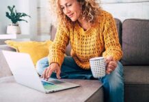 Woman on a couch using a laptop and holding a mug