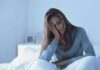 Woman sitting in bed looking tired with hand on face