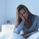Woman sitting in bed looking tired with hand on face
