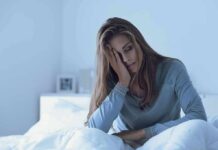How Sleep Chaos Supercharges Disease Risks Woman sitting in bed looking tired with hand on face