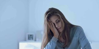 Woman sitting in bed looking tired with hand on face