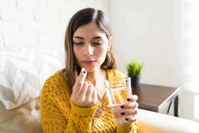 Woman holding a pill and a glass of water