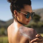 Woman in sunglasses applying sunscreen to her shoulder outdoors