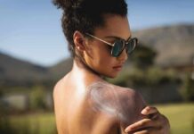 Woman in sunglasses applying sunscreen to her shoulder outdoors