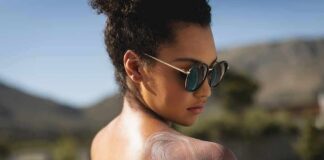Woman in sunglasses applying sunscreen to her shoulder outdoors
