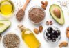 Assorted healthy fats with avocados, nuts, seeds, olives, and oils on a white background