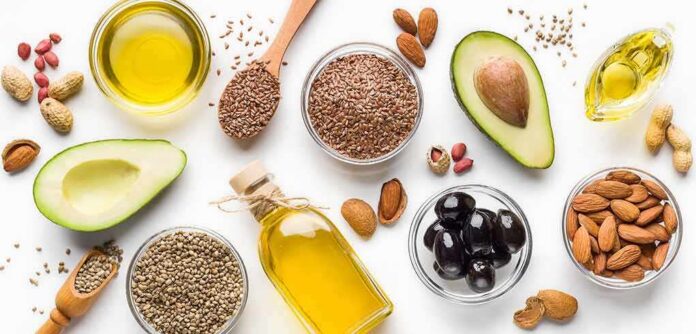 Assorted healthy fats with avocados, nuts, seeds, olives, and oils on a white background