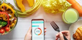 hands holding phone with calorie tracker beside salad and pastry