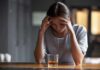 Woman with head in hands at a bar with a glass of whiskey