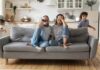 Parents sit on couch while children run around in living room