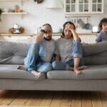 Parents sit on couch while children run around in living room