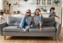 Parents sit on couch while children run around in living room