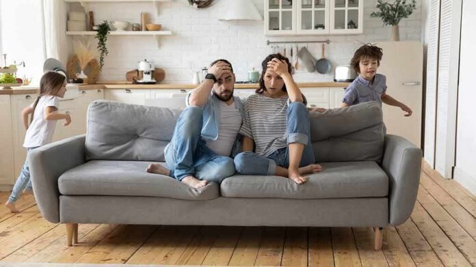 Parents sit on couch while children run around in living room