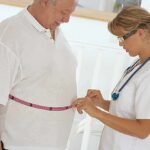 Healthcare worker measuring man's waist with tape