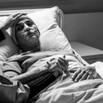 Patient in hospital bed with nasal oxygen held by visitor