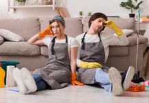 Two tired cleaners sitting on the floor by a sofa