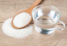 Glass of water beside wooden spoon filled with granulated sugar