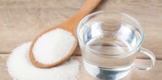 Glass of water beside wooden spoon filled with granulated sugar