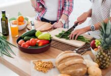 Hands chopping fresh herbs on a cutting board beside assorted produce