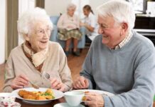 Two seniors smiling while eating a meal together at a table